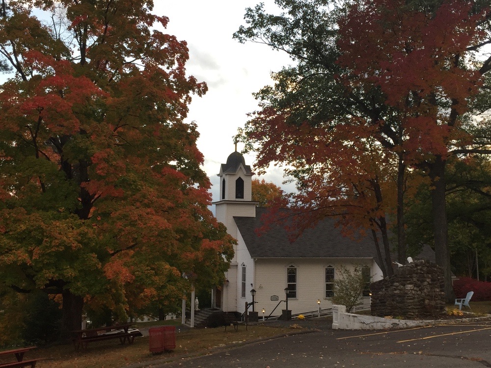 The white church on the hill in Fiskdale, framed by red and orange autumn trees.