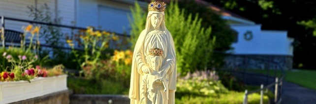 A crowned white statue surrounded by flowers on the shrine grounds.
