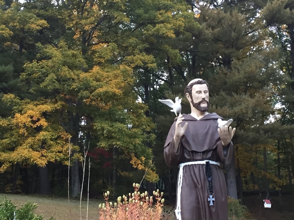 A statue of a friar among the trees on the shrine grounds.